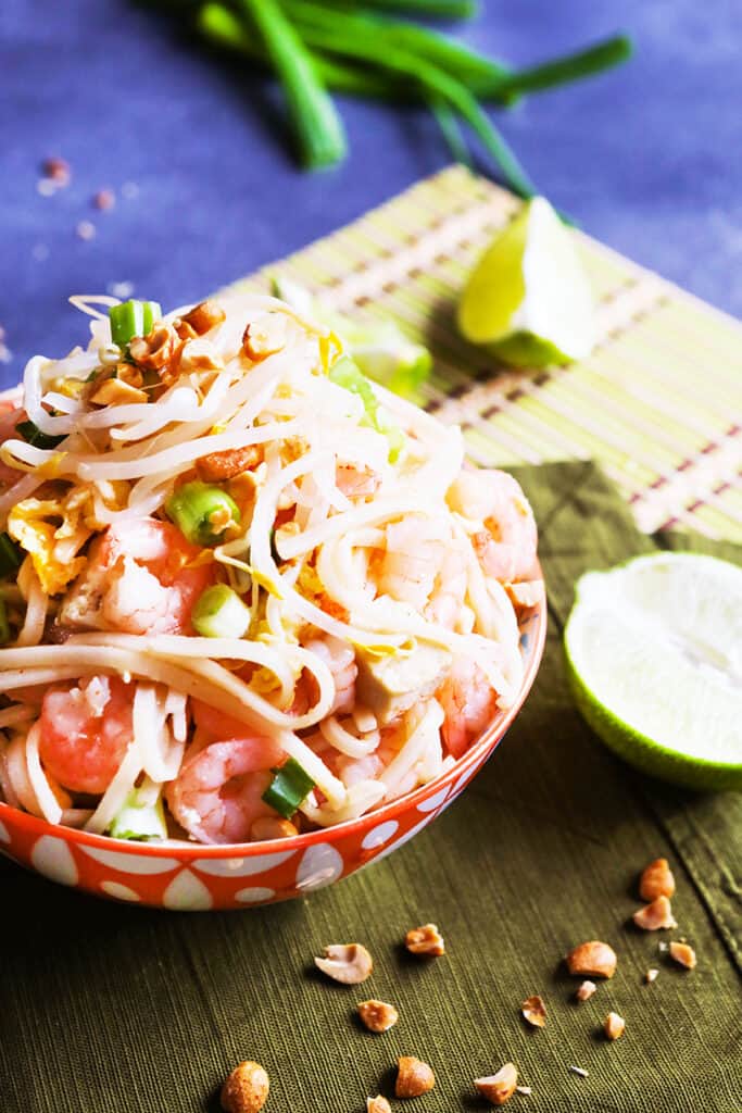 Shrimp and tofu pad thai in a bowl with half a lime on the side. 