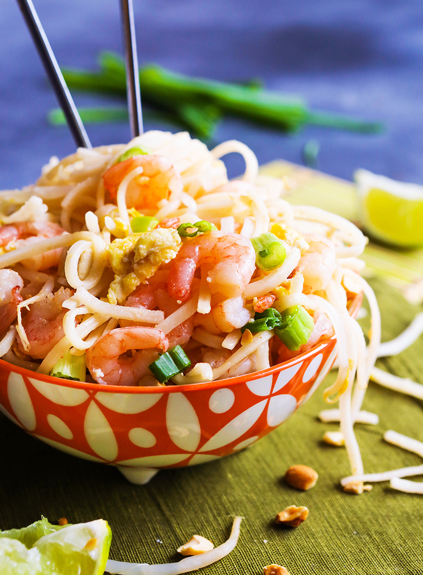 Chopsticks sticking out of a heaping bowl filled with shrimp pad thai.