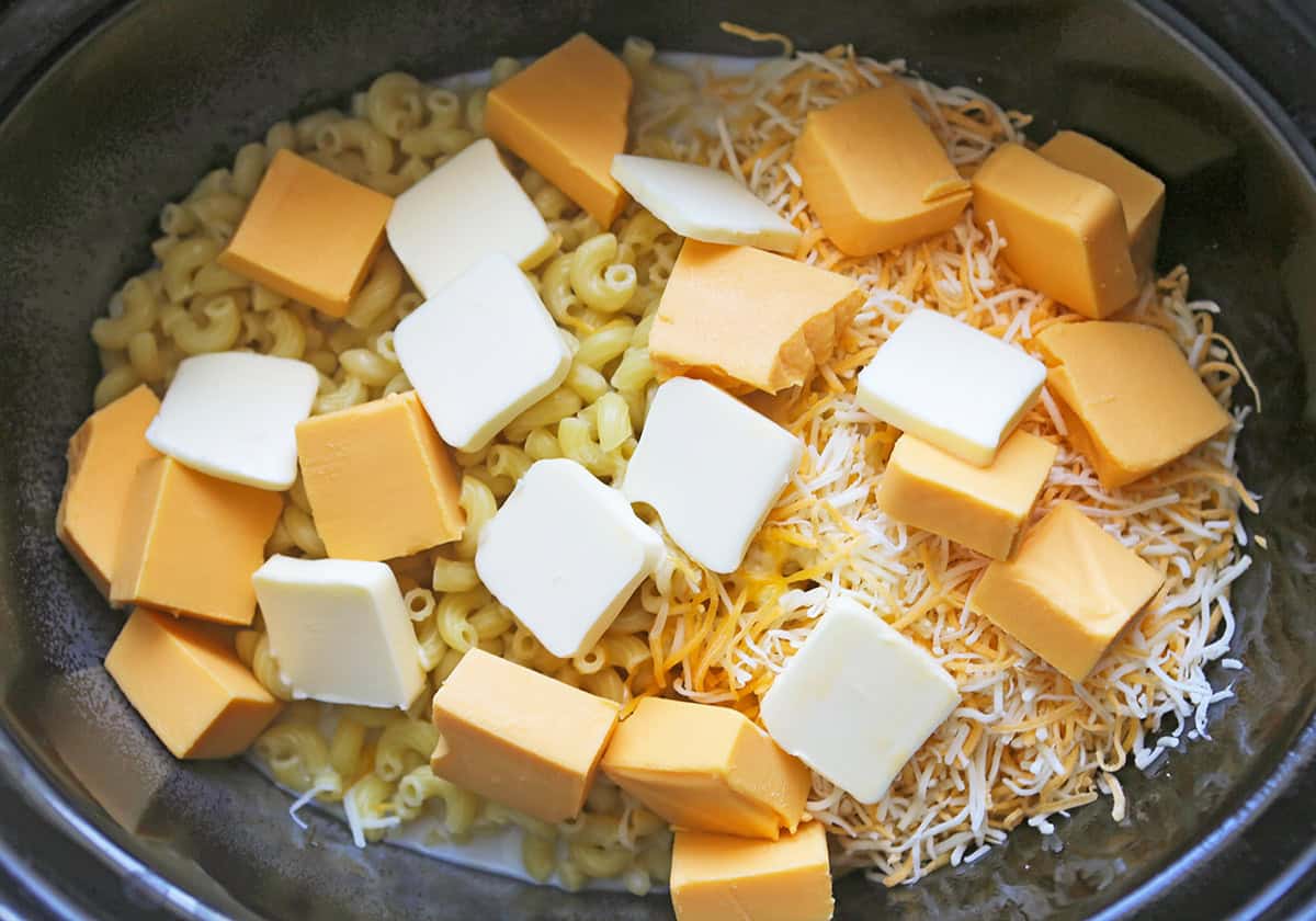 Uncooked mac and cheese with Velveeta cheese in a slow cooker.