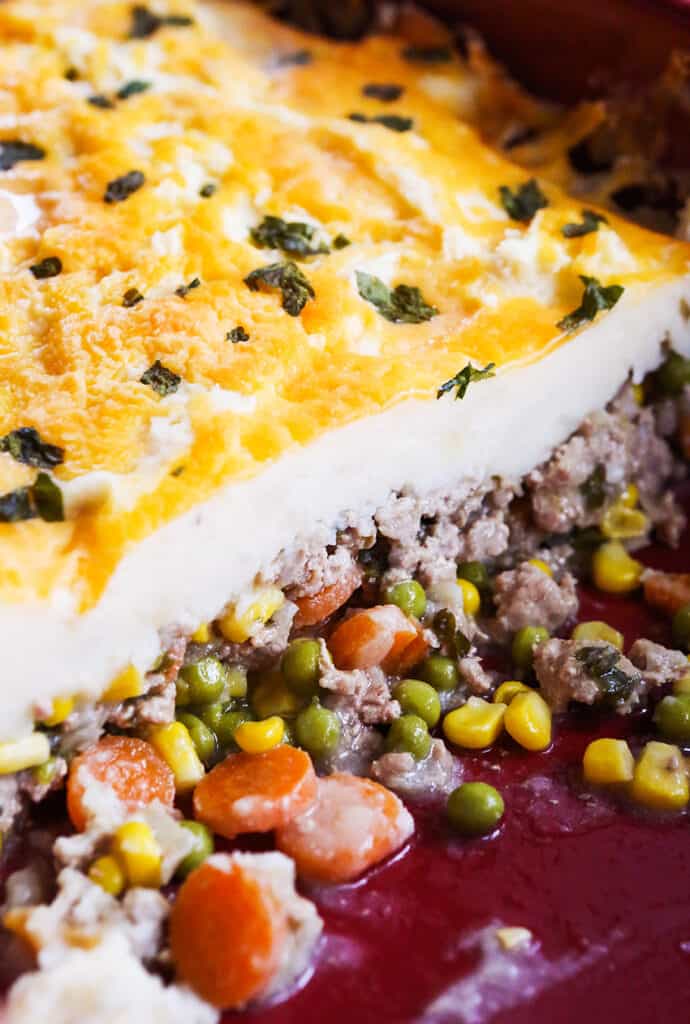 Turkey shepherd's pie in a casserole dish with veggies spilling out from under the mashed potatoes. 