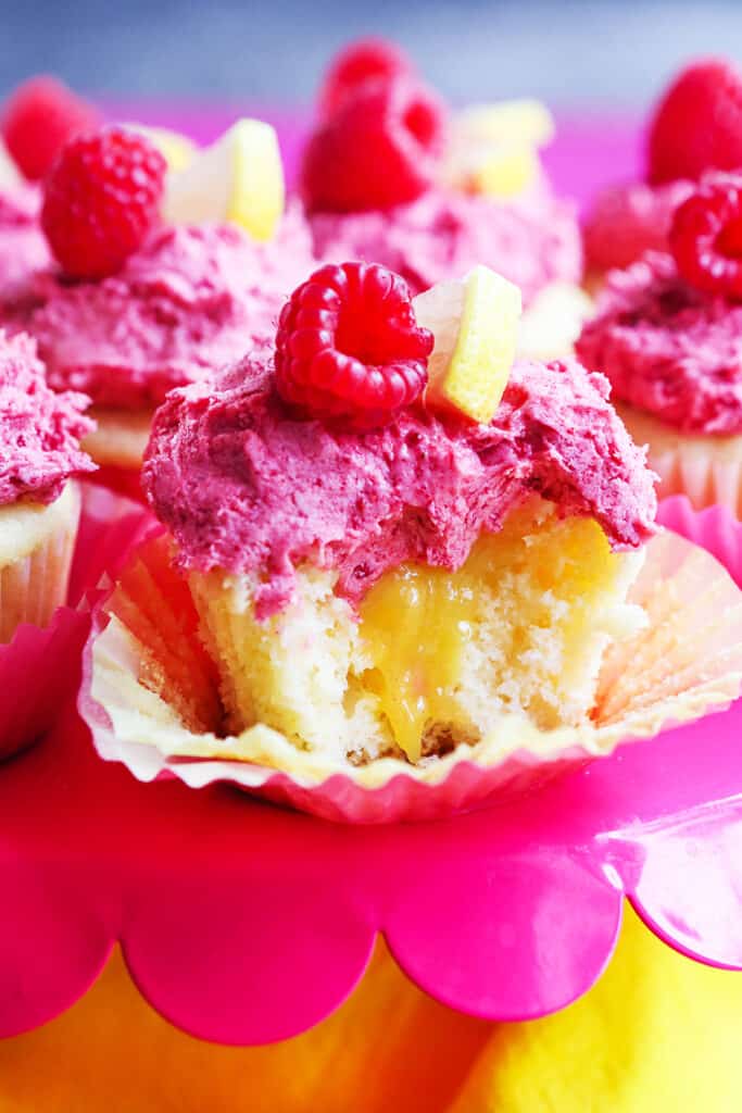 Lemon cupcake with curd falling out the center and topped with raspberry buttercream frosting.