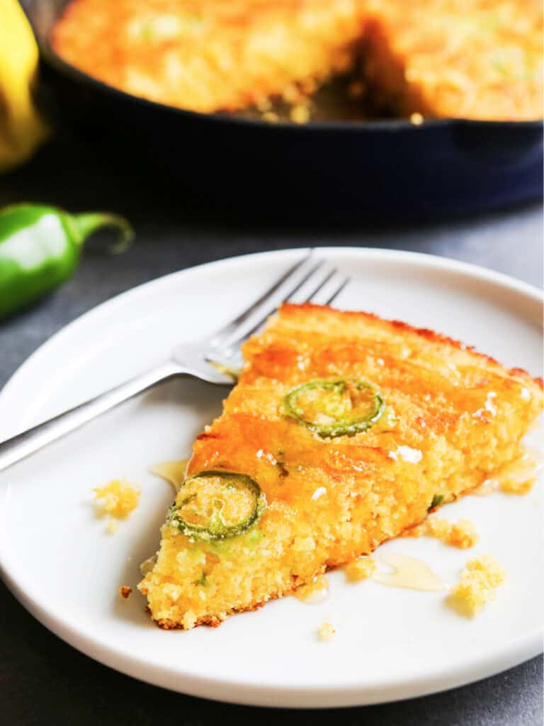 A slice of cheddar jalapeno cornbread sitting on a plate next to a fork. 