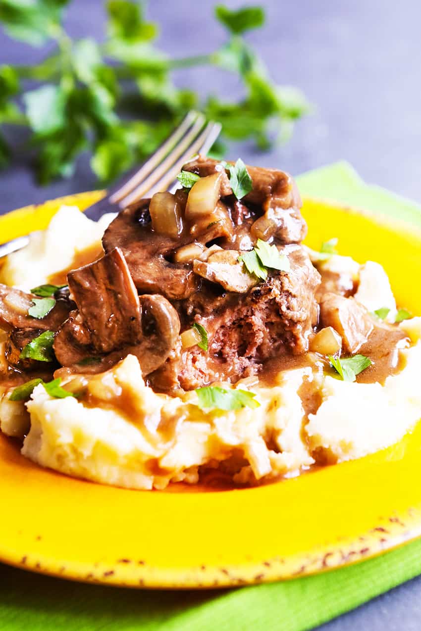 Salisbury steak and mushrooms atop a pile of mashed potatoes.