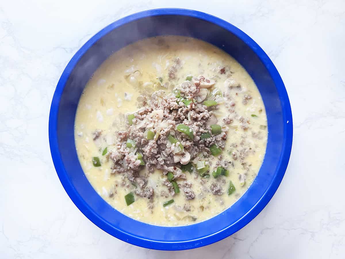 Egg mixture in a mixing bowl, with cooked sausage and veggie mixture in the middle.