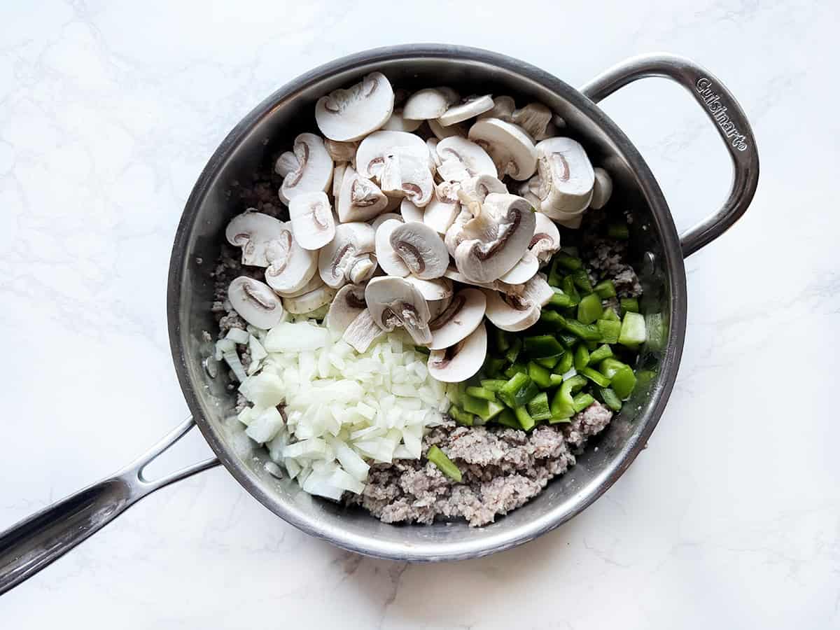 Mushrooms, onions, sausage and bell peppers in a skillet.