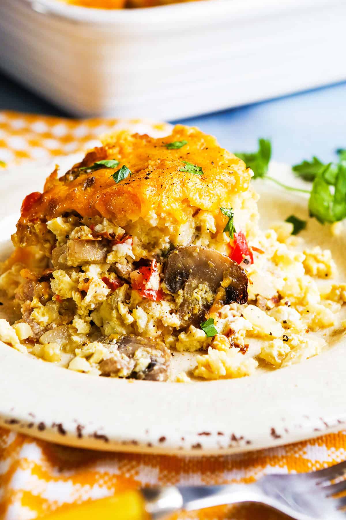 Close up of a serving of tater tot breakfast casserole on a plate, with parsley nearby.
