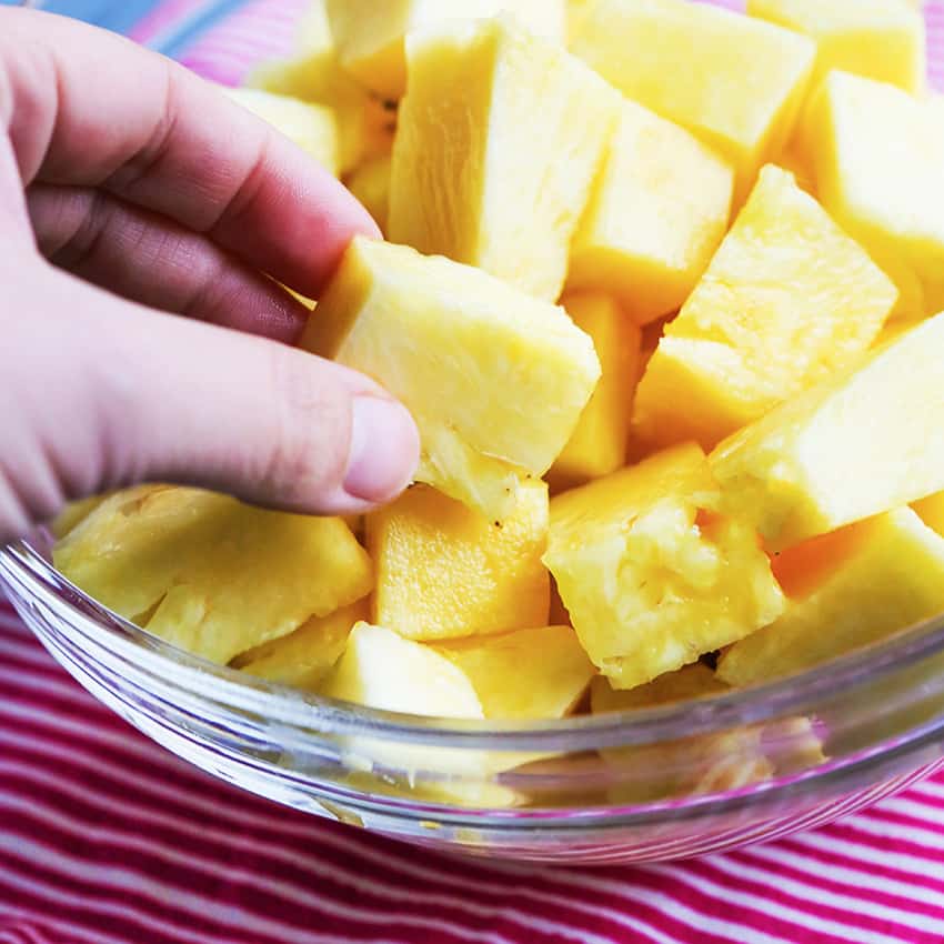 Hand picking up a chunk of freshly cut pineapple. 