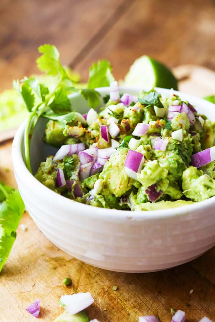 A bowl filled with guacamole and diced red onions topped on it. 