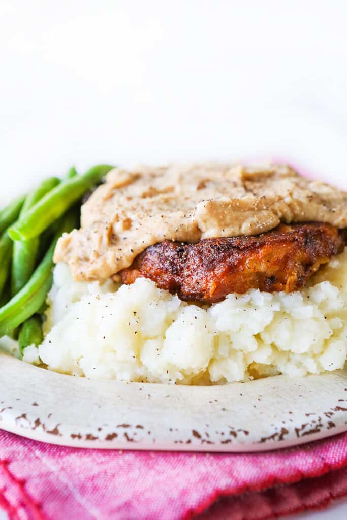 Chicken fried steak sitting on a plate of mashed potatoes and a side of green beans. 