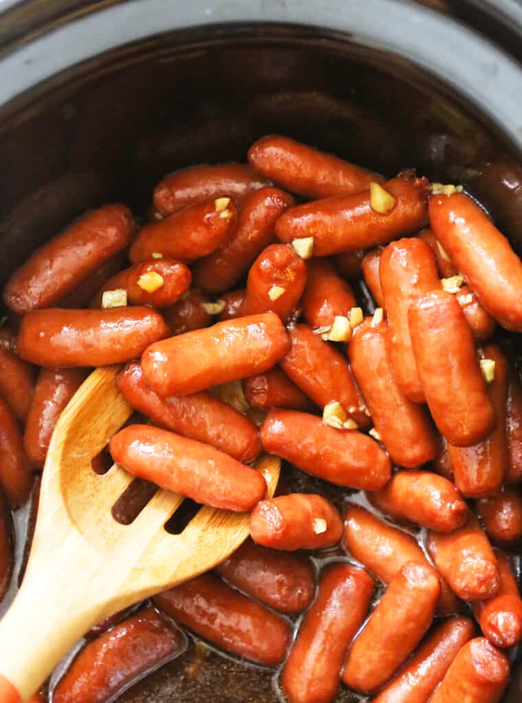 Serving spoon in a slow cooker filled with lil smokies in a honey garlic sauce. 