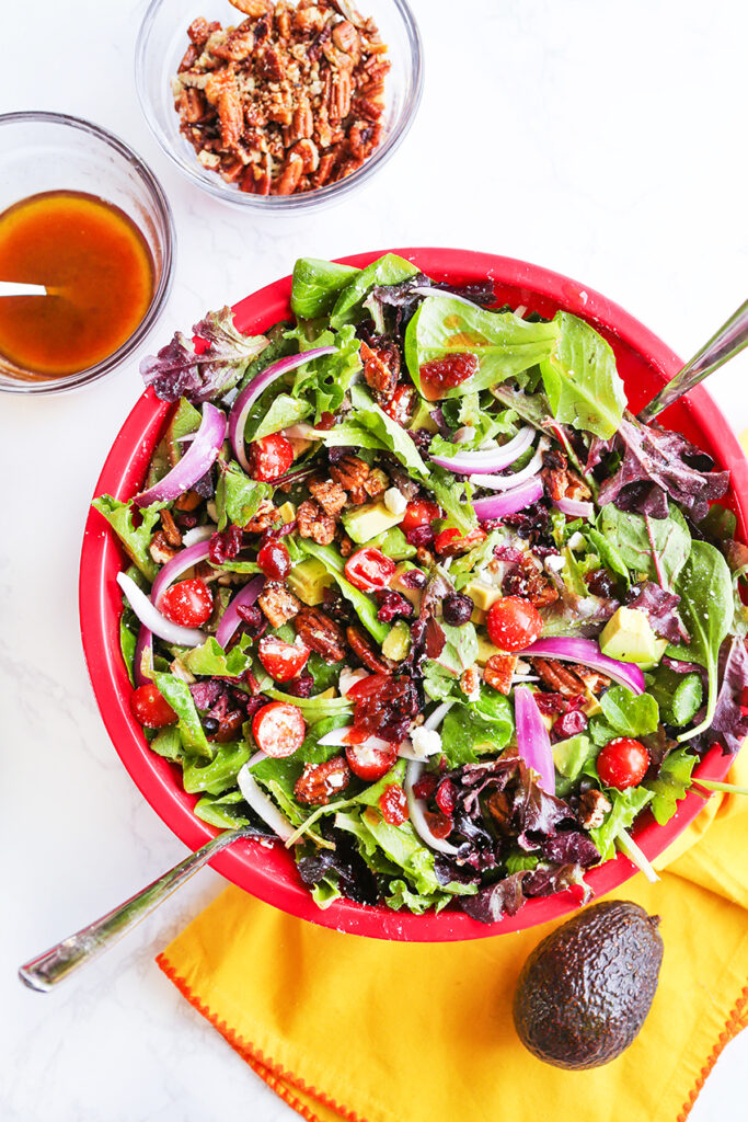 Large salad bowl filled with a chopped salad and two small bowls with dressing and candied pecans. 