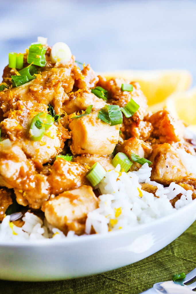 Rice and orange chicken in a serving bowl with diced green onions garnished on top. 