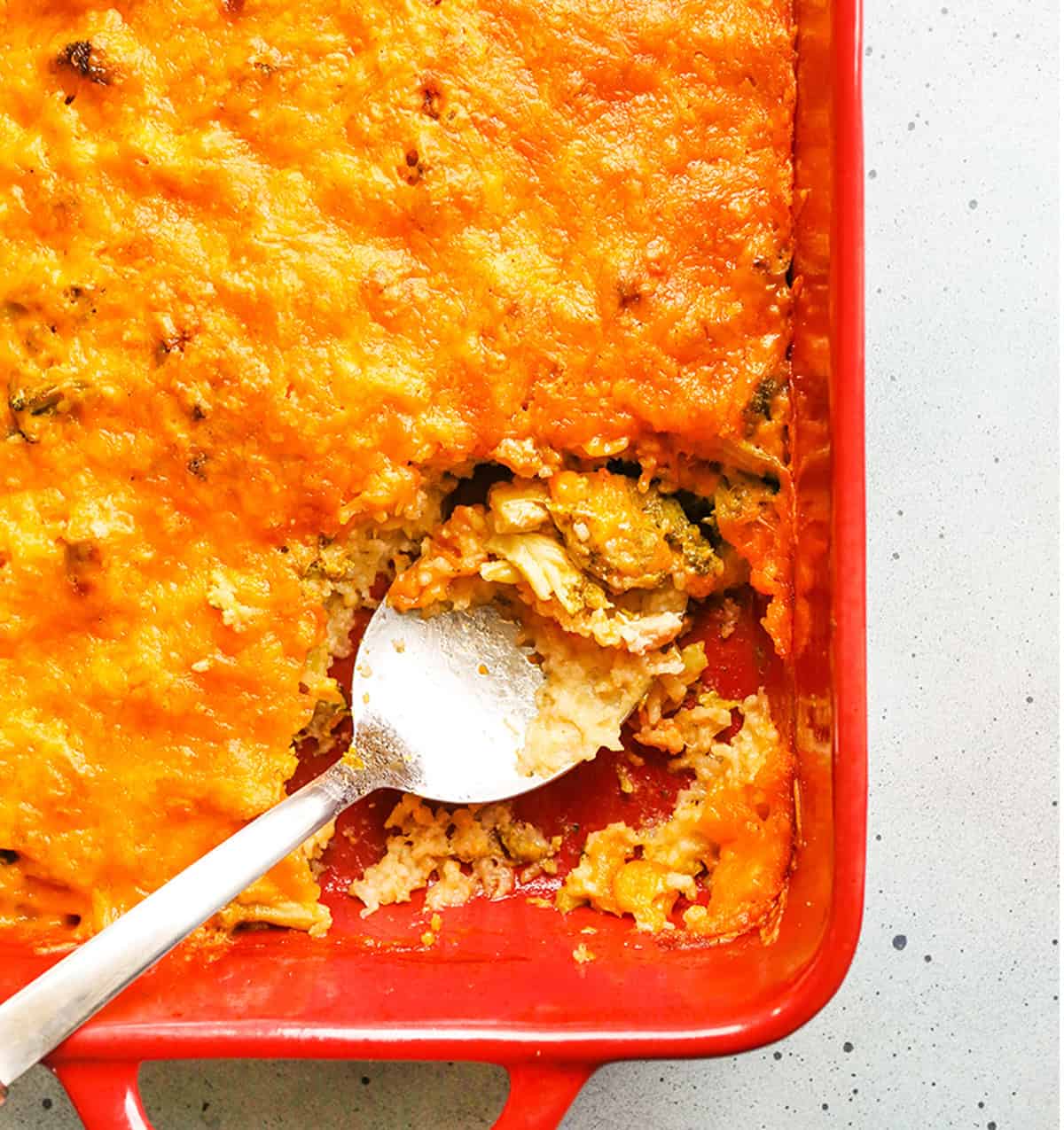 Serving spoon inside a cheesy casserole with rice and broccoli.