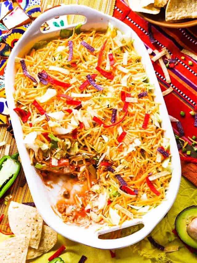 7 layer taco dip in a baking dish with some removed. 