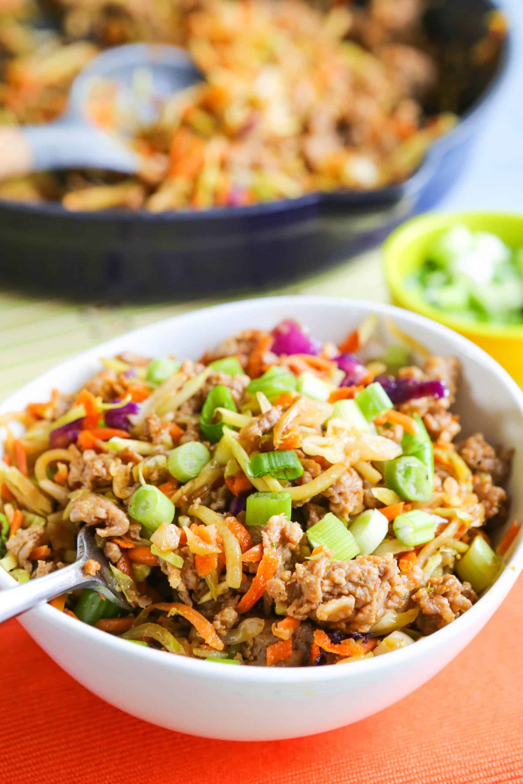 Egg roll in a bowl with coleslaw mix and green onions in a white bowl.