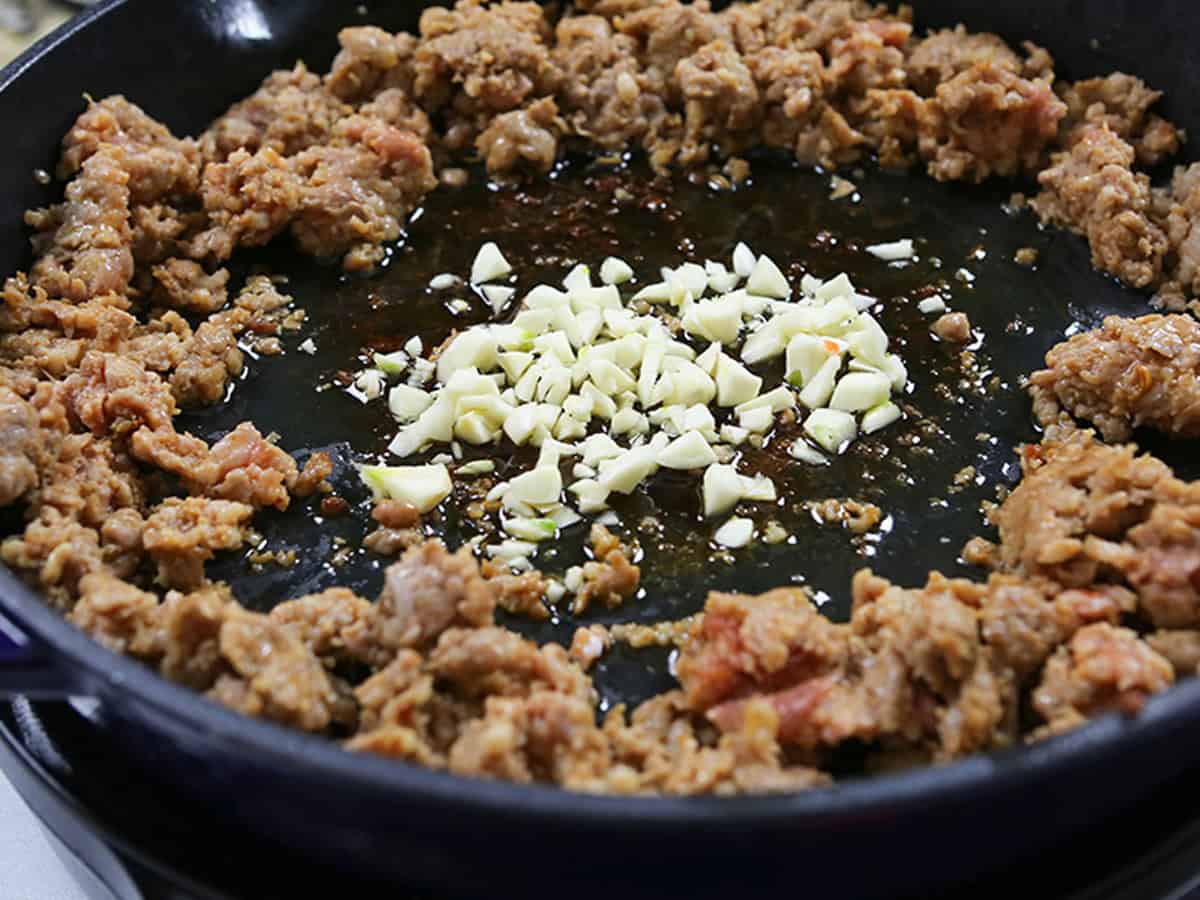 Cooking ground pork with garlic in a skillet for egg roll bowl.
