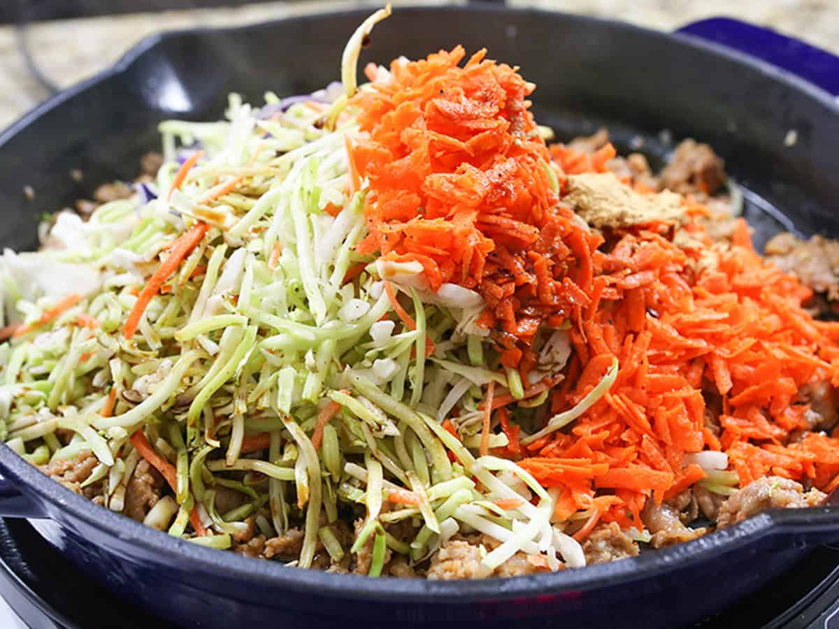 Egg roll in a bowl with shredded cabbage and carrots in a skillet.