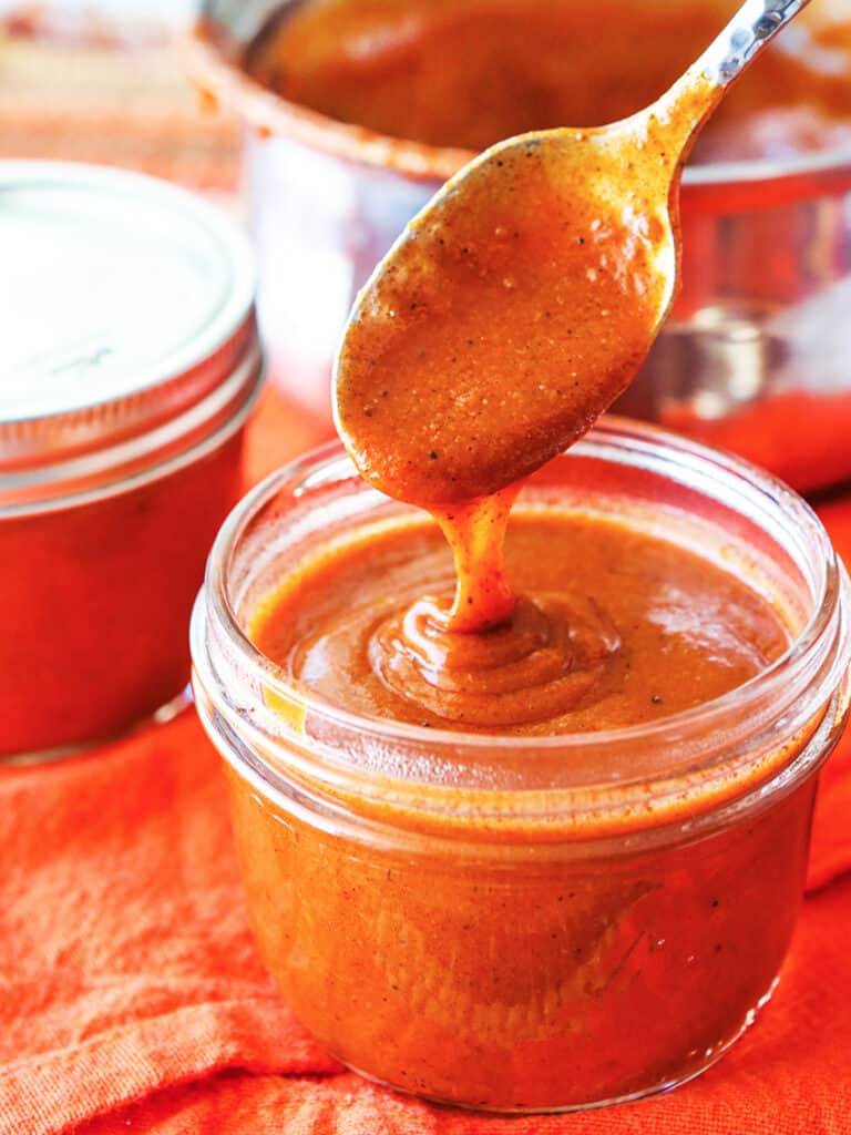 Spoon dripping homemade enchilada sauce into a mason jar