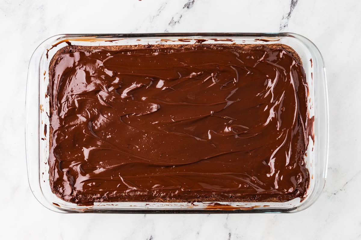 Shiny, smooth layer of chocolate spread evenly over brownies in a baking dish.