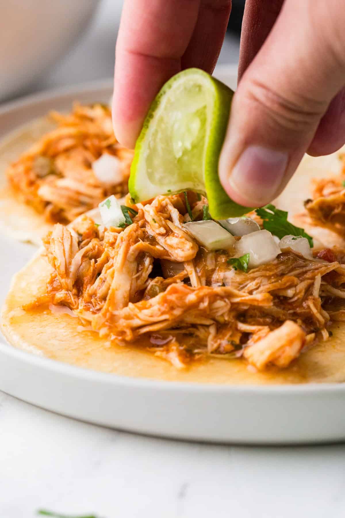 Fingers squeezing a lime over shredded chicken on tortillas.