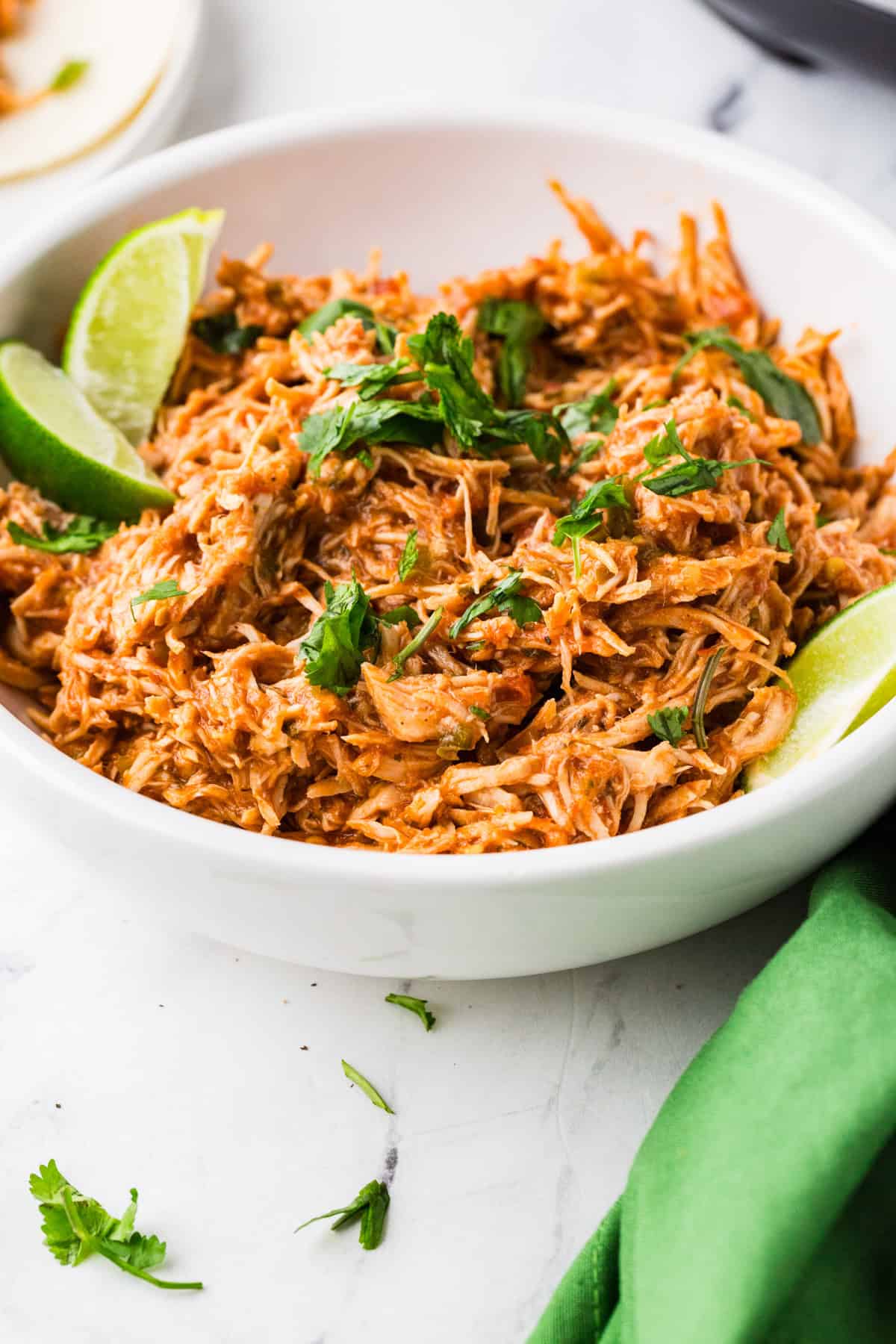 Serving bowl filled with shredded tender chicken, and two lime wedges nearby.