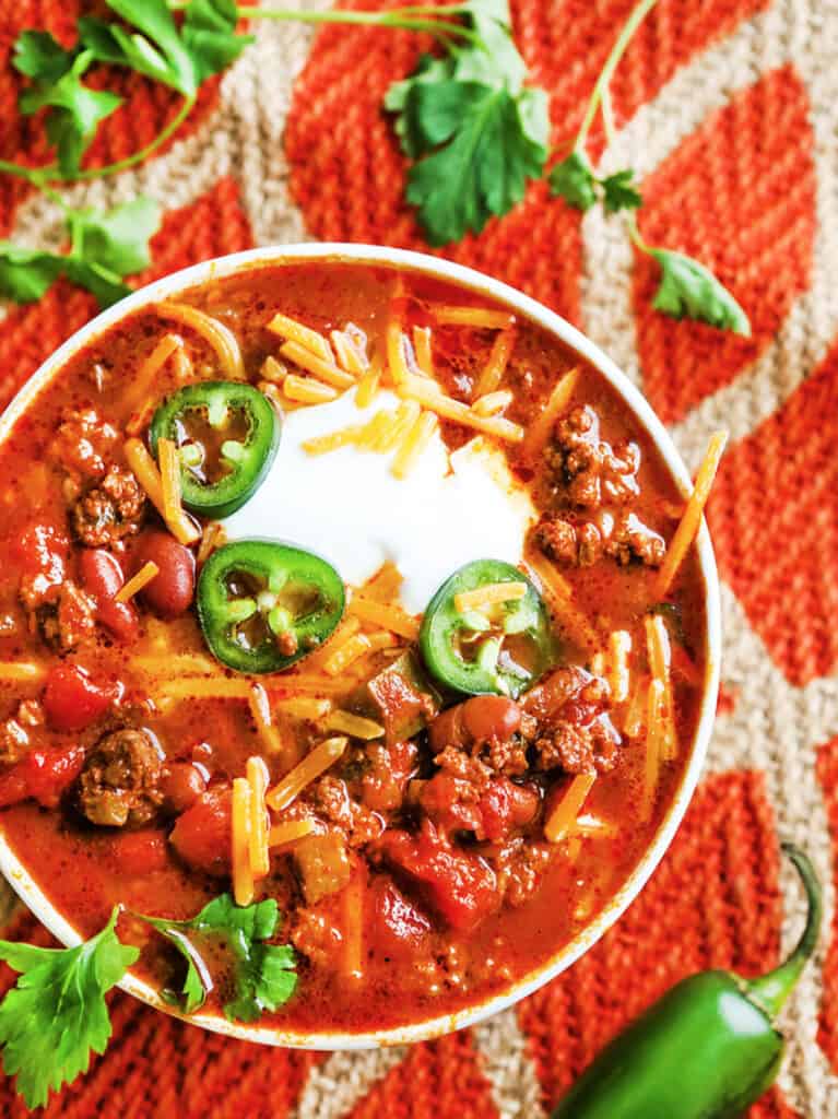 looking down into a bowl of chili with jalapeno slices, cheese and sour cream on top.