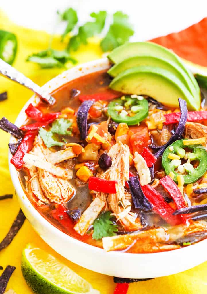 Bowl of chicken tortilla soup with slices of avocado and jalapeno rounds garnishing it and a spoon tucked into the broth. 