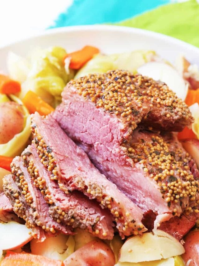 Plate of corned beef on a plate with potatoes and some veggies to the side. 