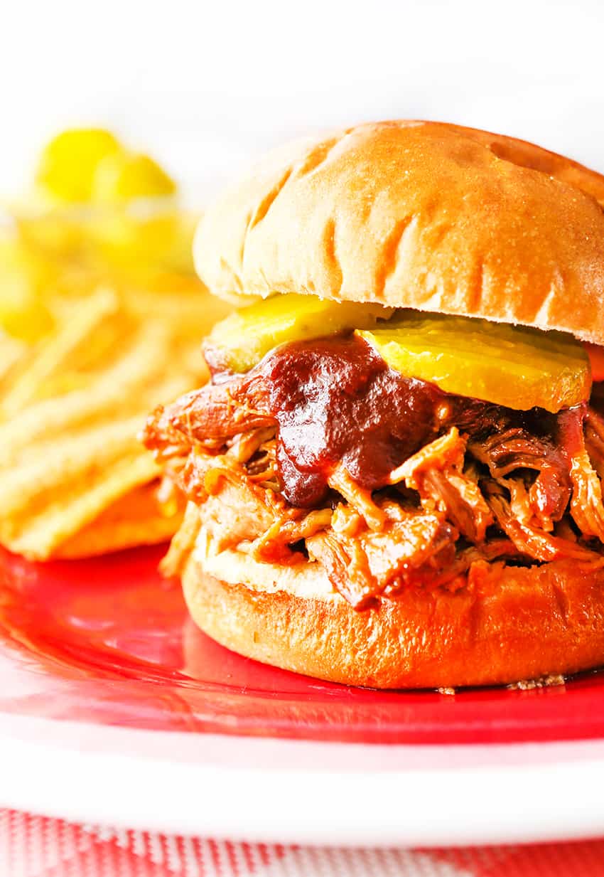 Pulled pork sandwich topped with bbq sauce and pickle slices.