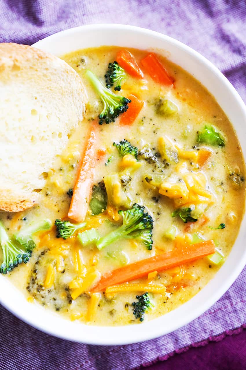 A piece of crusty bread sticking into a bowl of cheesy broccoli soup.