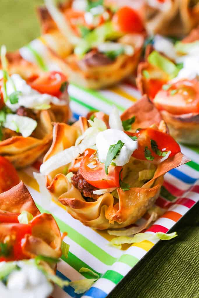 Taco cups filled with lettuce and tomatoes on a serving platter.