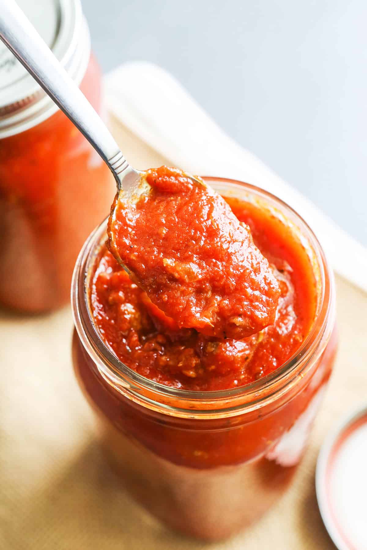 Spoon lifting pasta sauce out of a jar.