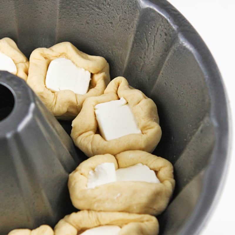 Unbaked monkey bread with cream cheese in a bundt pan.