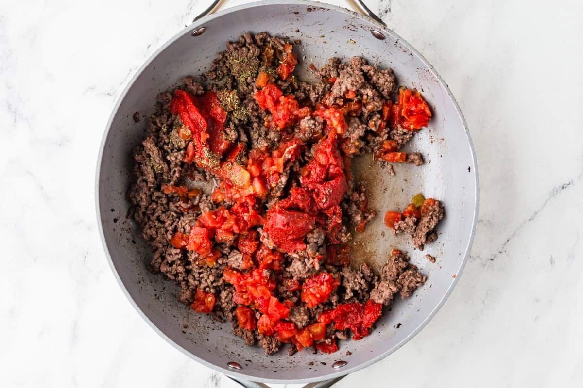 Top view of a skillet filled with cooked ground beef and tomatoes.