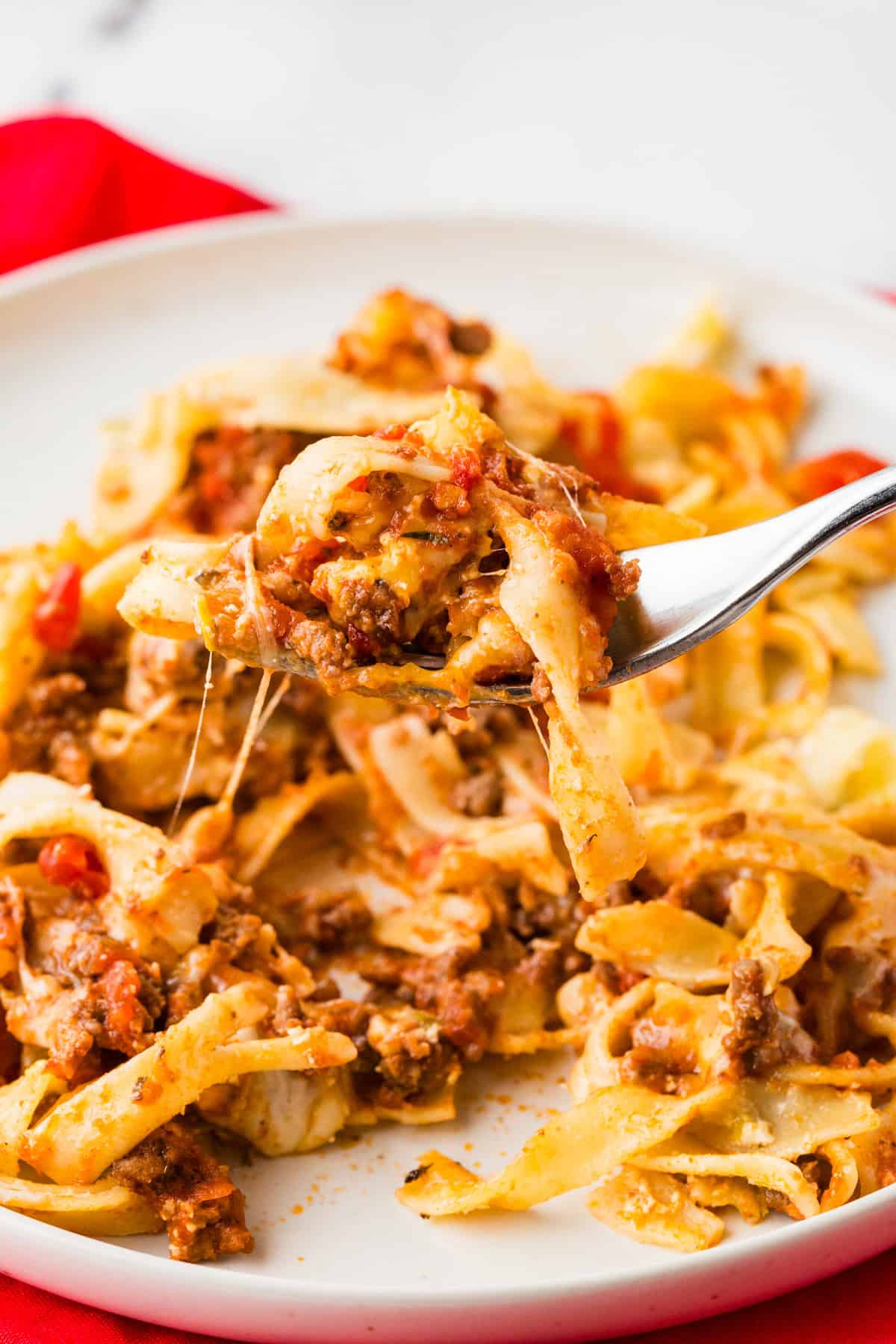 Fork lifting a bite of cheesy, beefy noodles from a plate.
