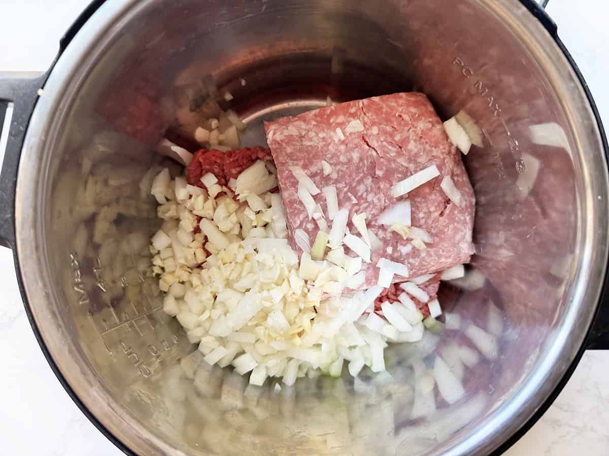 Ground beef and sausage in a pressure cooker with onions, ready to cook.