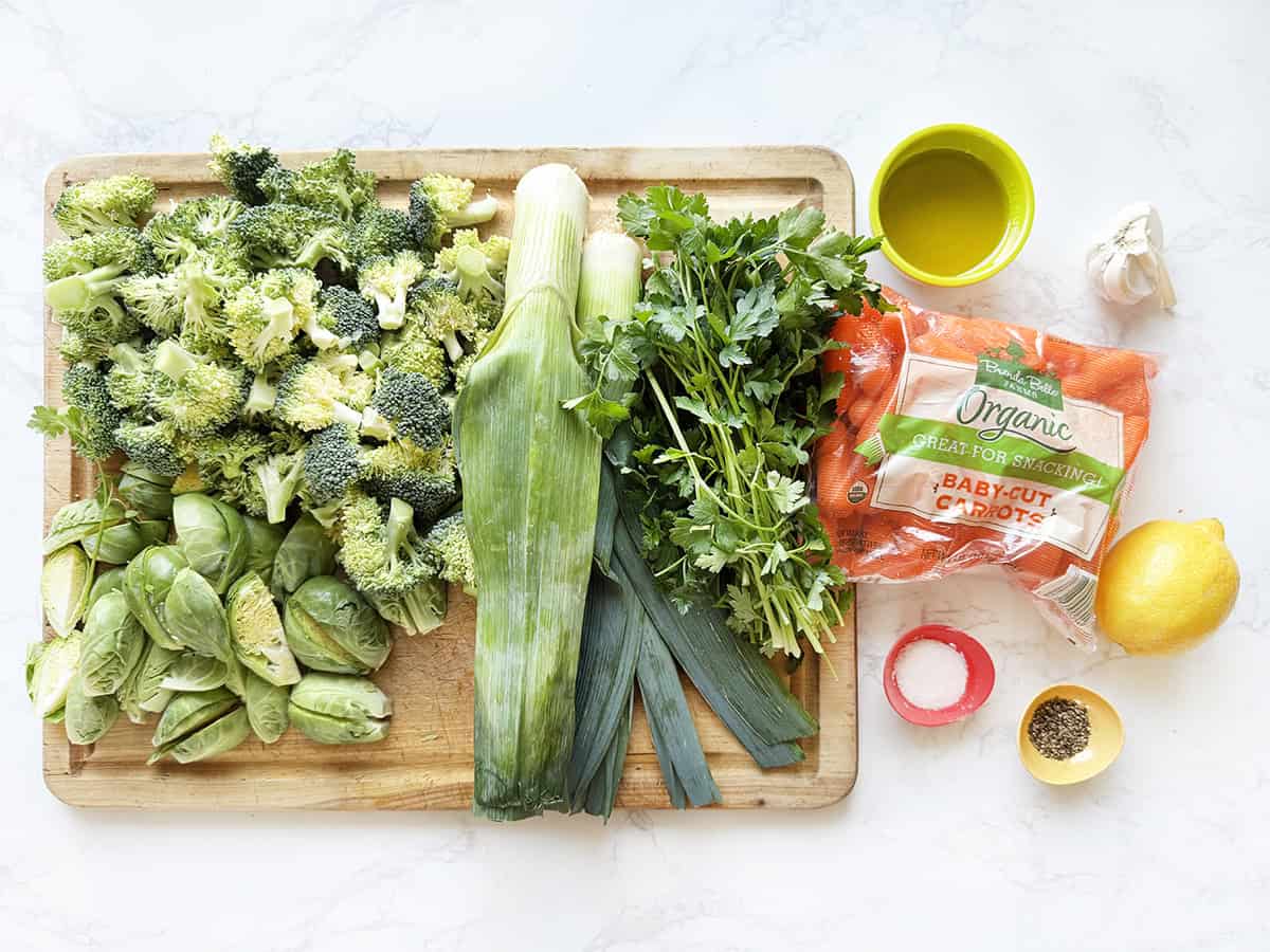 Chopped broccoli and brussels on a cutting board with leeks and other ingredients to roast vegetables.