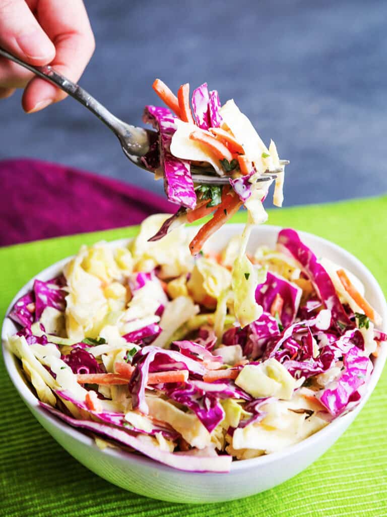 Fork full of coleslaw pulling out of a serving of coleslaw. 