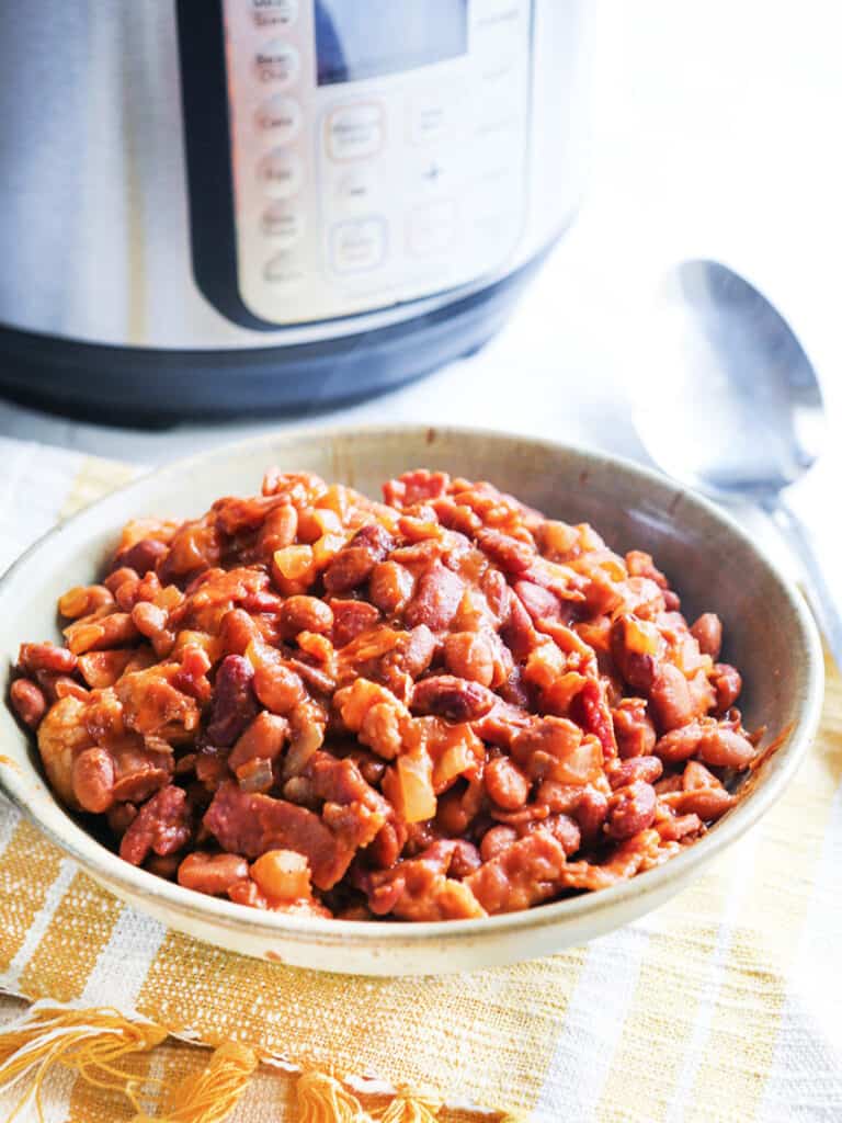 Serving bowl of instant pot baked beans next to an Instant Pot.