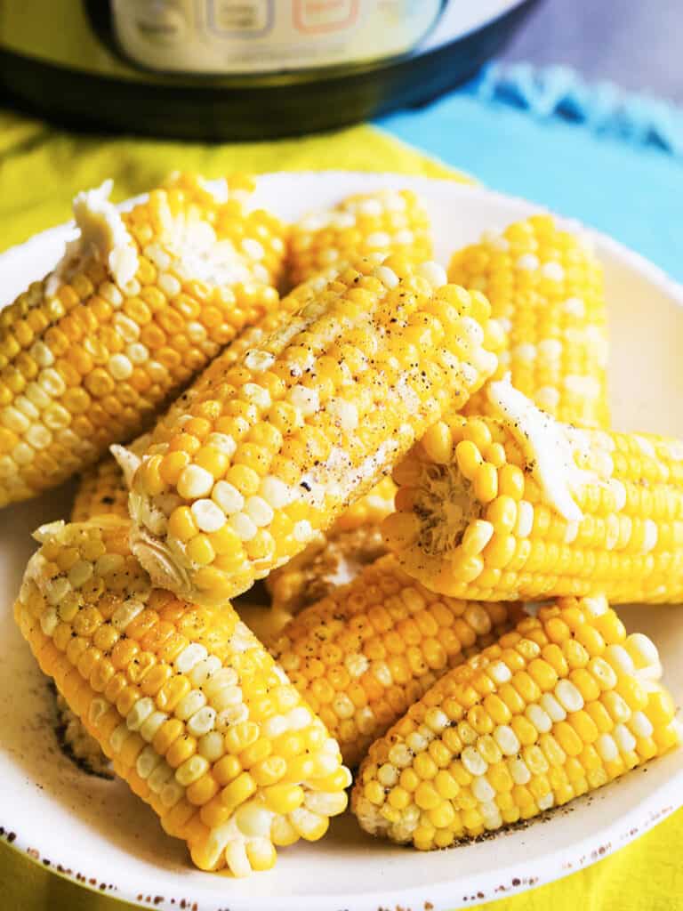 corn on the cob stacked on a serving plate with butter and pepper