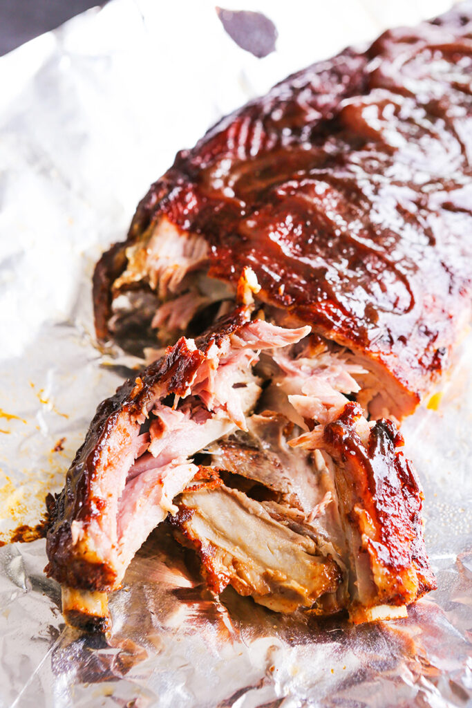 instant pot ribs with bbq sauce slathered on top and one rib with the meat shredded off the bone