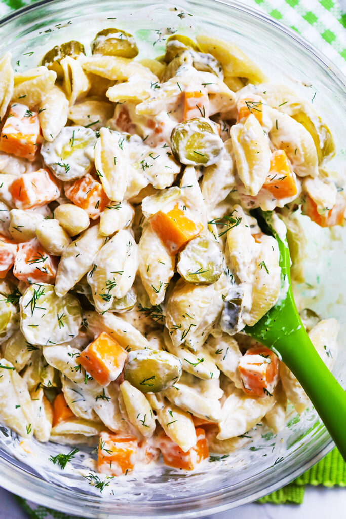 Dill pickle pasta salad in a bowl with a green serving spoon inside. 