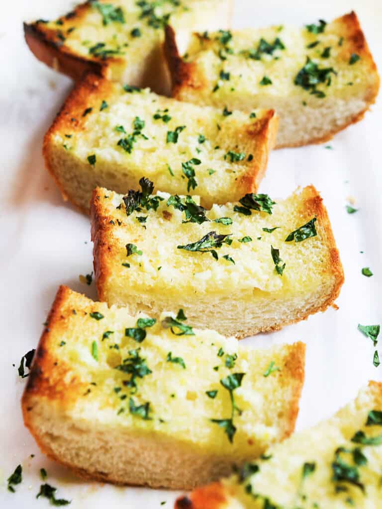 Garlic bread french bread garnished with parsley on a platter. 