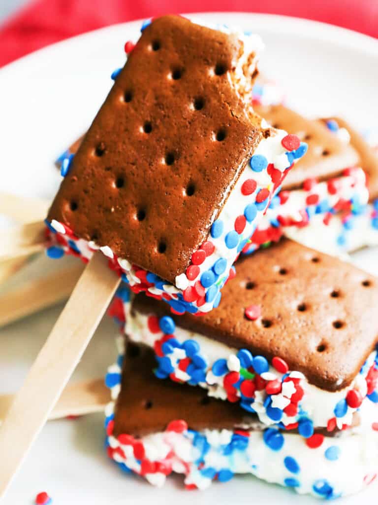 red and white sprinkles on ice cream sandwiches with sticks placed on a plate together