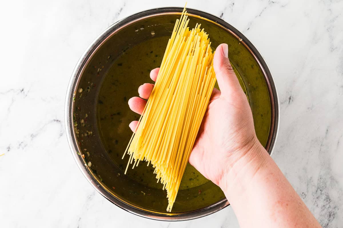 Hand holding dry pasta over pot.