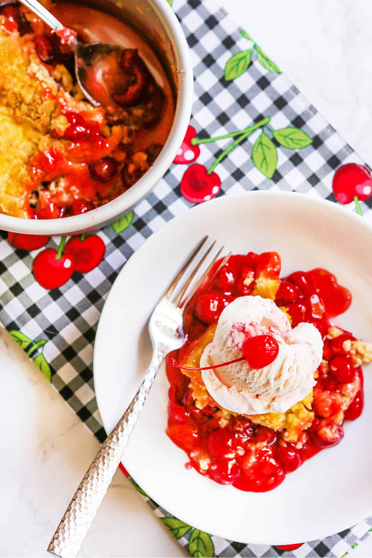 Cherry cobbler topped with vanilla ice cream and fresh cherries on a white plate.