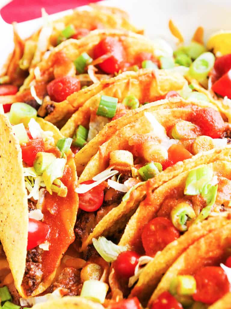 pan of tacos filled with toppings lined up and standing on end in a baking dish.