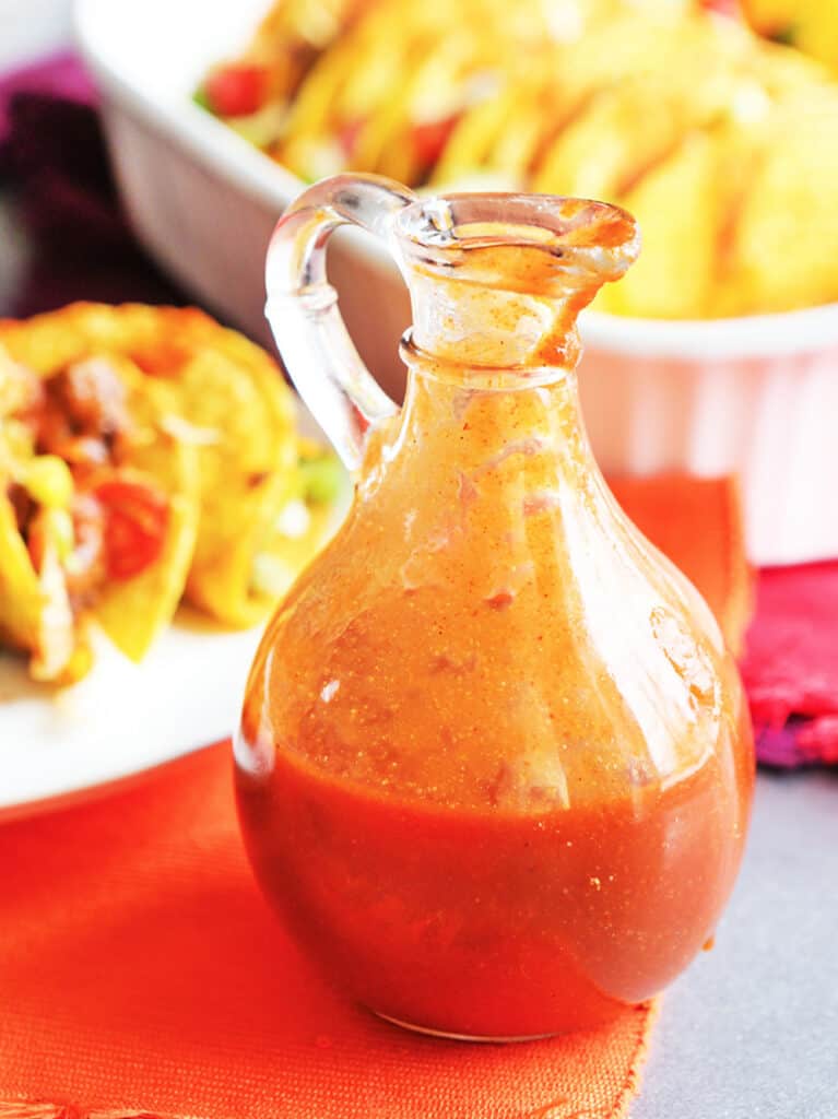 Taco sauce in pourable container sitting next to plate of tacos