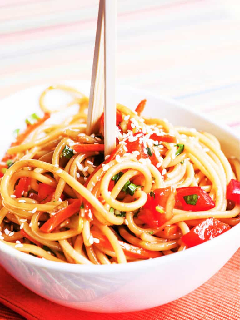 Asian pasta salad in a serving bowl with chopsticks jabbed int