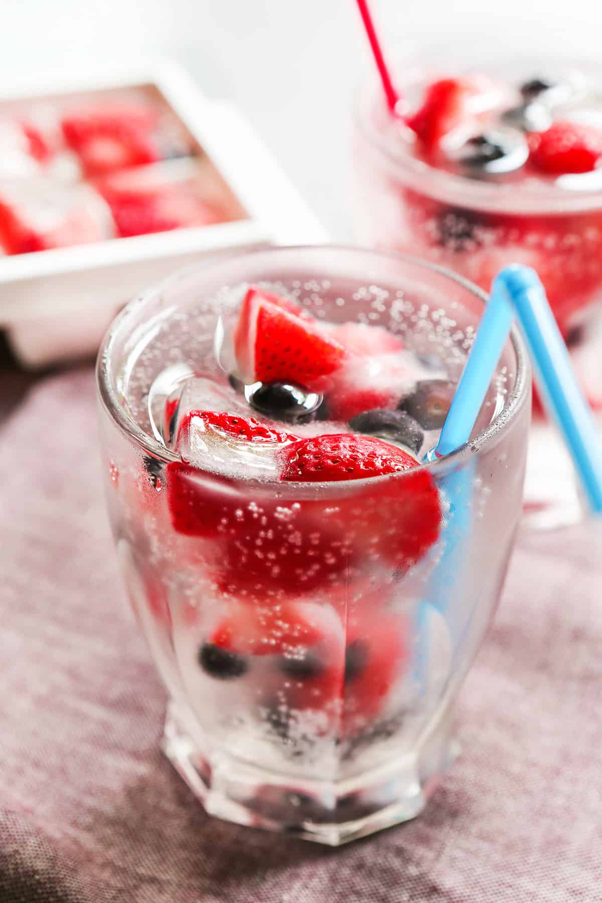 Glass of water with fruit cubes inside and a straw sticking out of the glass.